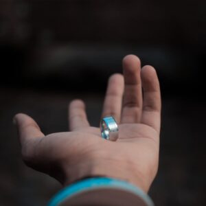 Close-up of a silver ring on an outstretched hand during a marriage proposal outdoors.