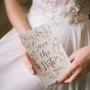 A close-up of a bride holding an elegant 'Save the Date' card with intricate calligraphy.